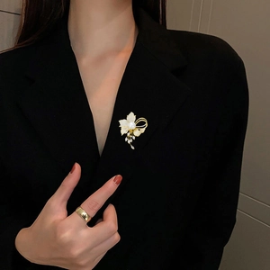 Detailed close-up of golden floral brooch with white zircons and hanging tassels on black blazer