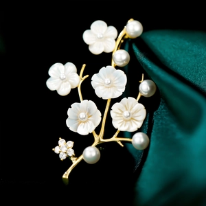 Elegant floral shell brooch with white pearls and gold branches on green silk fabric