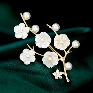 Elegant gold flower brooch with white shell petals and pearls on green velvet background