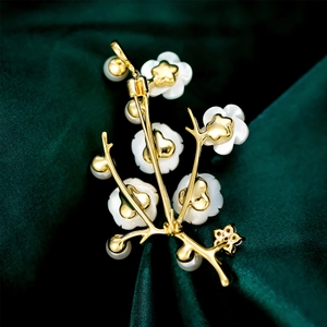 Macro shot of a gold floral brooch with shell petals and pearls on green silk fabric