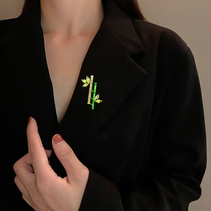 Bamboo shaped brooch with green enamel and marquise green gems on a black suit lapel