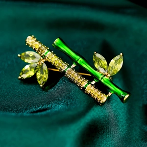 Elegant bamboo brooch with green enamel and sparkling crystals on silk background