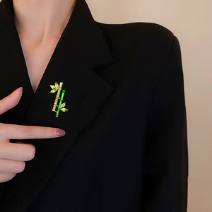 Detailed bamboo brooch with green enamel and emerald crystals on a black suit lapel