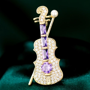Elegant violin brooch with gold plating, purple gemstones and pearls on green velvet
