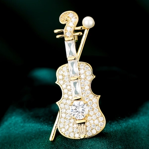 Macro shot of violin brooch with sparkling zircons and pearl on green silk fabric