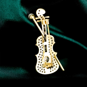 Close-up of gold violin brooch with micro-pave crystals on green silk fabric