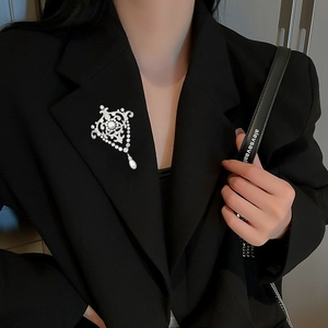 Détail macro d'une broche perle vintage avec zircons sur le revers d'un blazer noir
