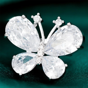Elegant silver butterfly brooch with teardrop gemstones on dark green silk background