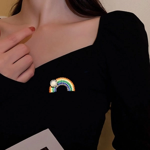 Detailed view of a rainbow brooch with a daisy accent pinned on a black fabric suit coat