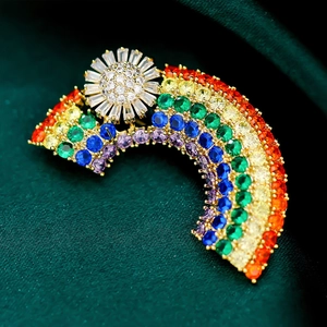 Close-up of a rainbow brooch with colorful zircons on dark green satin fabric background