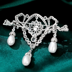 Macro shot of silver crystal brooch with fringe pearls on dark green satin fabric