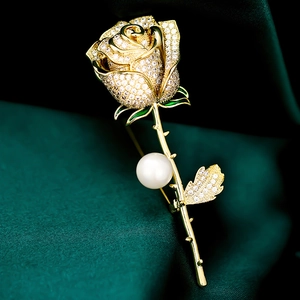 Macro view of gold rose brooch with sparkling diamonds, white pearl and green enamel