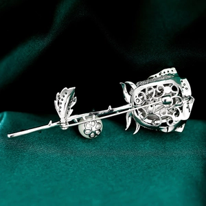 Macro detail of a silver rose brooch with micro-pave crystals and a white pearl accent