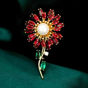 Elegant sunflower brooch with red gems and central pearl on a green velvet surface