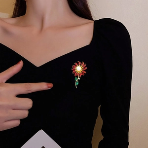 Close-up of a sunflower brooch with red zircon petals and white pearl on a black coat