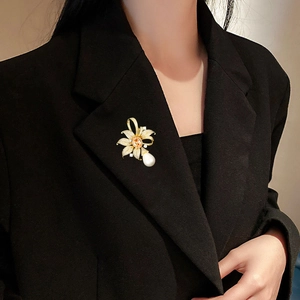 Détail d'une broche fleur dorée ornée de cristaux et d'une grande perle en goutte