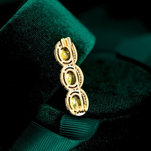Detailed view of gold triple oval brooch with yellow-green stones on green velvet box