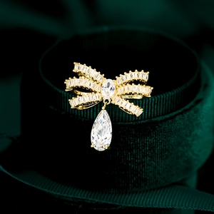 Elegante spilla a fiocco dorata con pendente in zircone su fondo di velluto verde scuro