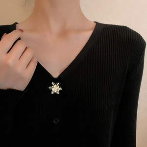 Close-up of a rotating gold snowflake brooch with zircon crystals on a black sweater