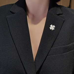 Detailed view of a four-leaf clover brooch with heart-cut zircons on a black blazer lapel