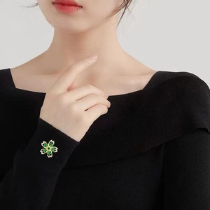 Broche fleur de cerisier dorée élégante avec zircons vert émeraude sur tricot noir