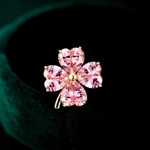 Macro detail of a four-leaf clover brooch featuring four pink heart-shaped crystals