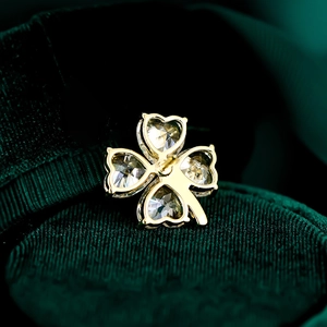 Macro view of a gold clover pin with heart-cut crystals on dark green velvet