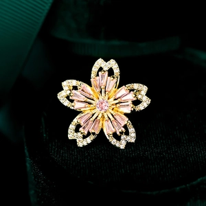 Broche fleur de cerisier dorée avec zircons roses sur fond de velours vert foncé
