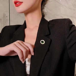 Nahaufnahme einer silbernen Brosche mit smaragdgrünem Stein auf einem schwarzen Blazer
