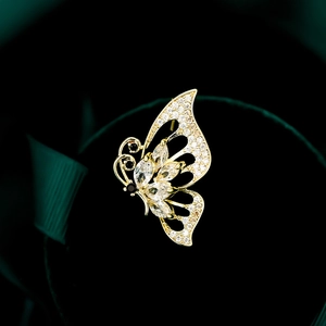 Elegant gold hollow butterfly brooch with marquise gems on dark green velvet background