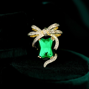 Macro detail of luxury bow pin with emerald green step-cut zircon in gold finish