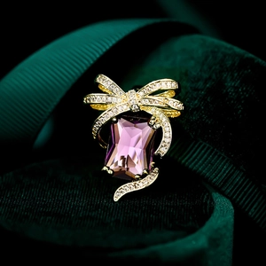 Macro shot of a luxury bow brooch with a large purple rectangular gemstone and gold details