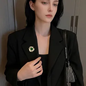 Spilla a vortice dorata con zircone verde su risvolto di blazer nero da donna