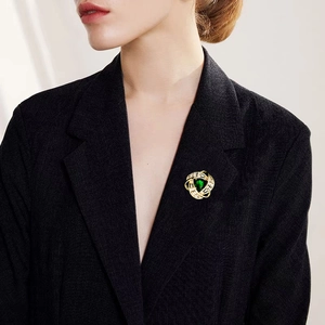 Elegante spilla a vortice dorata con zircone verde smeraldo e cristalli su un blazer nero