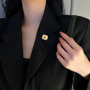Detalle de broche de circón amarillo cuadrado con pavé de cristales sobre blazer negro