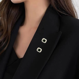 Primer plano de broches cuadrados verde esmeralda con circonitas en solapa de blazer negro