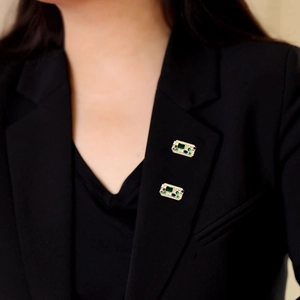 Detailed view of emerald and blue stone brooches pinned on a black blazer lapel