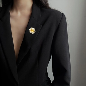 Detailansicht einer eleganten Blumenbrosche mit gelbem Edelstein auf schwarzem Sakko