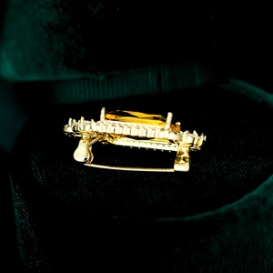 Makroaufnahme einer Goldbrosche mit großem gelben Ovalstein und Kristall-Halo-Detail