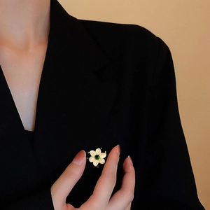 Elegant gold flower brooch with green center gemstone on black blazer lapel