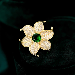 Macro shot of luxury gold flower brooch with pavé petals and large green gemstone