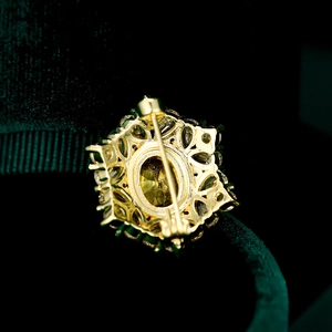 Makroaufnahme einer Vintage-Goldbrosche mit Sicherheitsnadel auf grünem Samtfutter