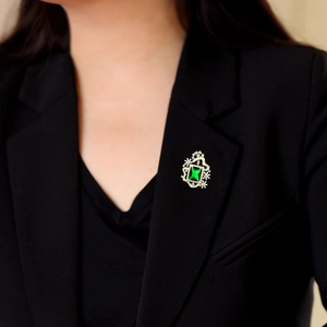 Broche vintage con piedra verde corte esmeralda y circonitas sobre un blazer negro