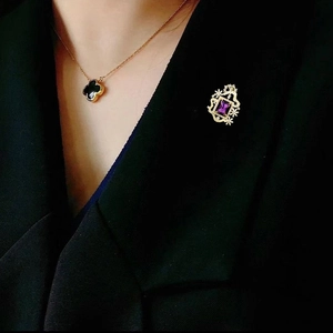 Elegante broche dorado con piedra púrpura y collar de trébol sobre blazer negro