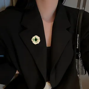 Vue détaillée de la broche fleur avec pierre vert émeraude sur un revers de veste noir