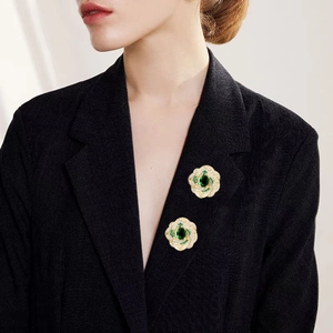 Détail d'une broche florale avec pierres vertes et cristaux sur un blazer noir élégant