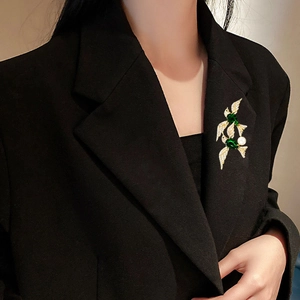 Detail of bird brooch with emerald green gems and micro-pave diamonds on black blazer