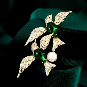 Macro shot of twin birds brooch with green wings, white zircons and a pearl detail
