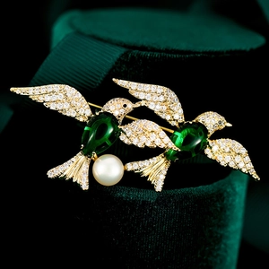 Macro shot of twin birds brooch with green crystals and pearl on velvet base