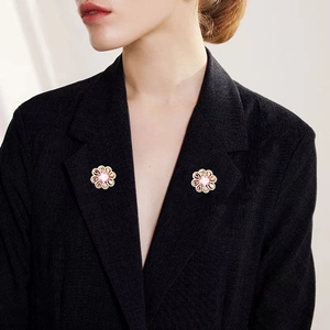 Detailed close-up of two pink flower brooch pins with zircons on a black blazer lapel